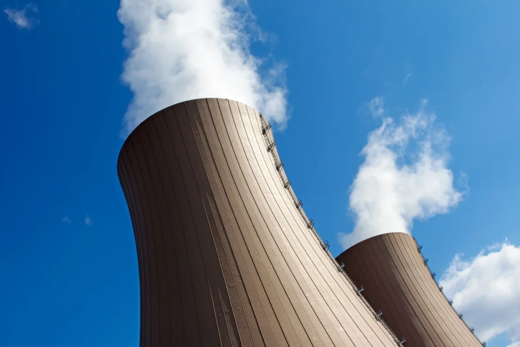 Tall nuclear cooling towers emitting steam against a clear blue sky, emphasizing radwaste management and industrial operations.