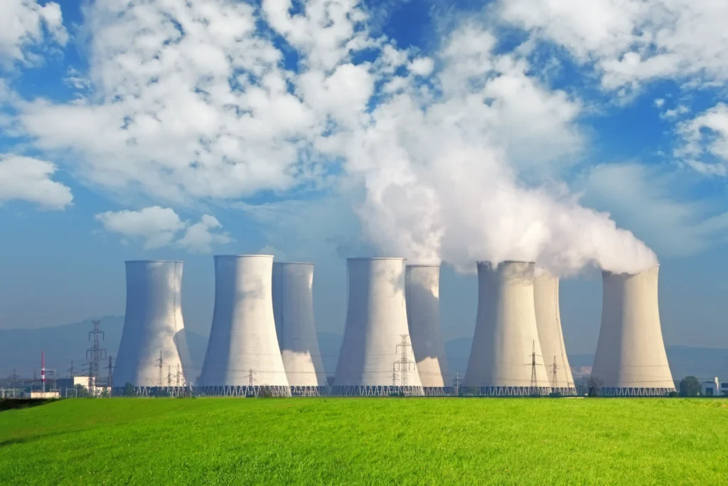 Cooling towers of a nuclear power plant emitting steam, set against a green field and blue sky, highlighting radwaste management and environmental impact.